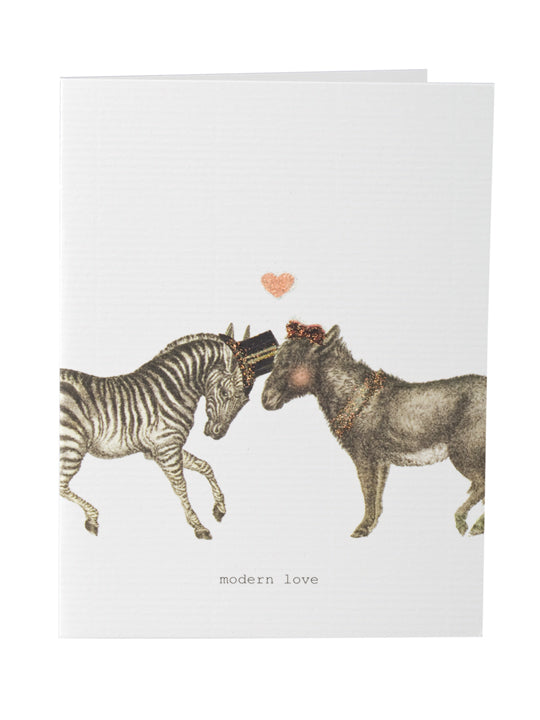 A TokyoMilk Greeting Card with an illustration of a zebra and a donkey nuzzling each other under a small pink heart, labeled "modern love" at the bottom, and hand-glittered accents