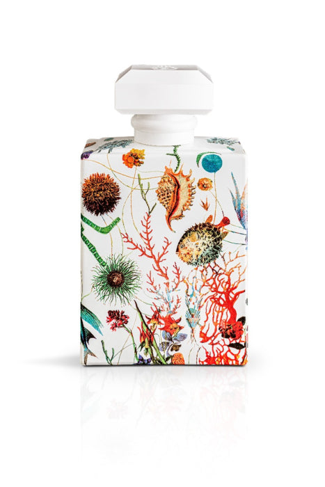 A Carthusia I Profumi de Capri perfume bottle with a unique, white botanical print featuring colorful illustrations of various flowers, leaves, and marine elements from the Capri garden, standing against a plain white background.