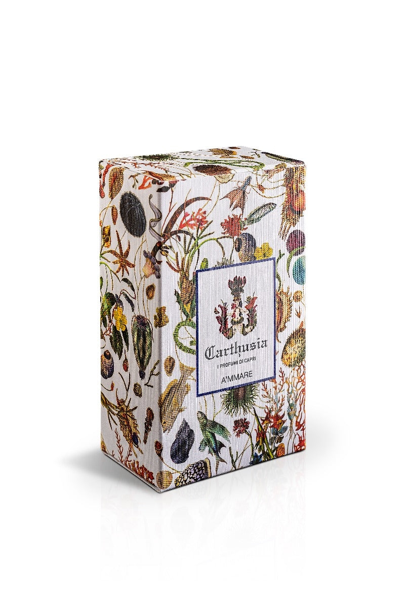 A square tea tin with a Capri garden print featuring various leaves, flowers, and fruits, labeled with the name "Carthusia A'mmare Eau de Parfum 50ml" in an elegant font on a centered white label. Brand Name: Carthusia I Profumi de Capri