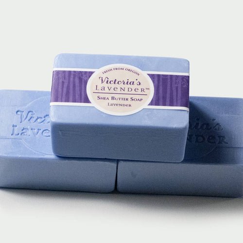 Three bars of Victoria's Lavender - Lavender Shea Butter Luxury Bar Soap, handmade and ideal for sensitive skins, colored in varying shades of purple, stacked against a white background. Brand name: Victoria's Lavender.