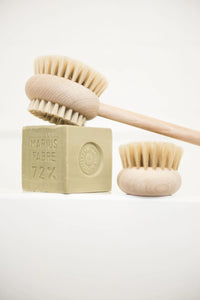 Two Andrée Jardin Beechwood Handle Bath & Body Brushes and a bar of soap labeled "marius fabre 72%" displayed against a white background. One brush is a French body brush.