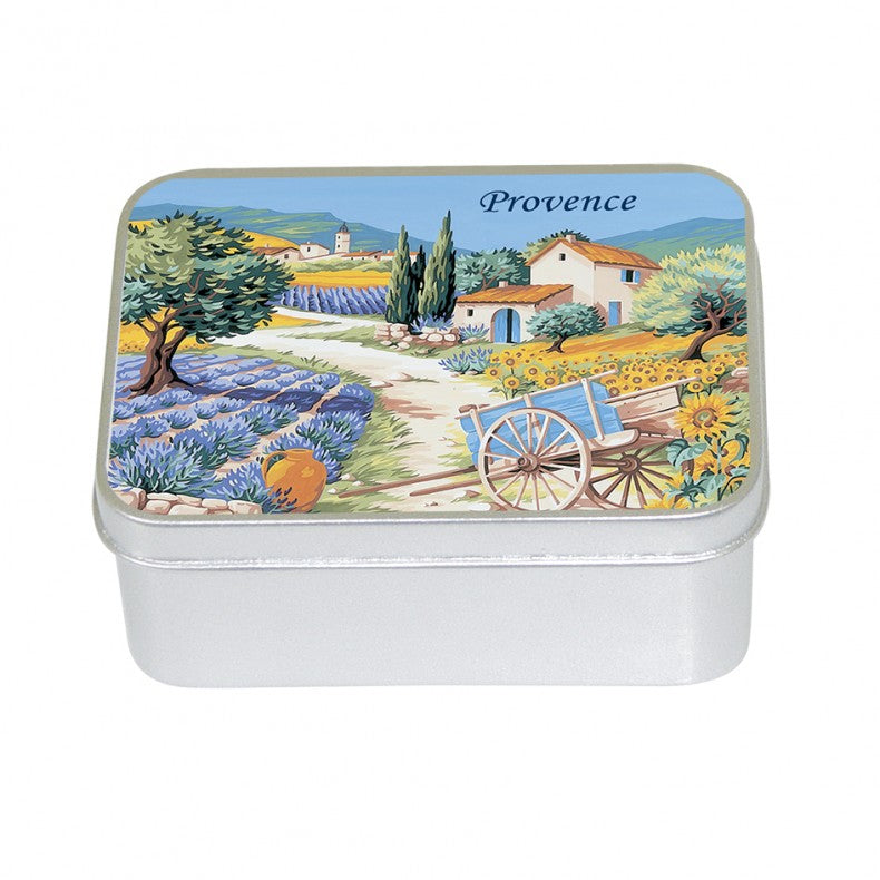A rectangular tin box with a colorful illustration on its lid depicting a scenic view of Provence countryside, featuring perfume lavender fields, a farmhouse, and a cart contains Le Blanc Provence Village Lavender  100gm Soap Tin by Le Blanc Made in France.