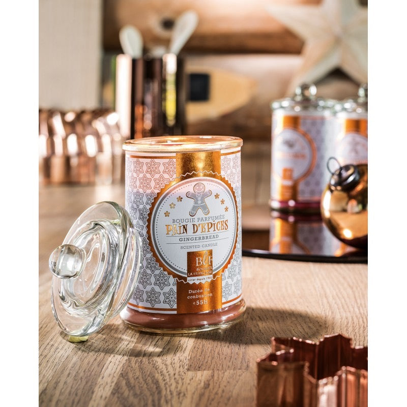 A Bougies la Francaise Large Scented Candle in Glass Candy Jar - Gingerbread on a wooden kitchen counter, accented by soft lighting and accompanied by Christmas candle in the background.