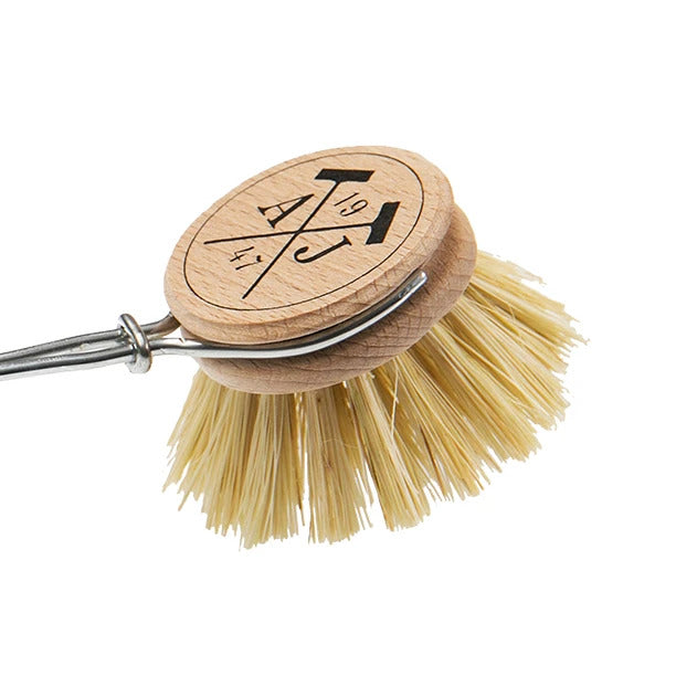 A Andrée Jardin Tradition Handled Dish Brush with a round, wooden handle engraved with symbols, connected to stiff, natural fiber bristles and a metal loop at the end.