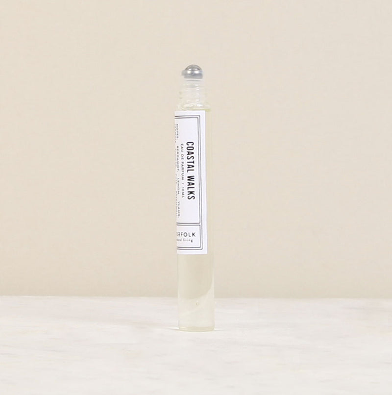 A clear rollerball perfume bottle labeled "Parfum de l'eau Coastal Walks" by Norfolk Natural Living, designed for unisex appeal, standing upright against a neutral beige background.