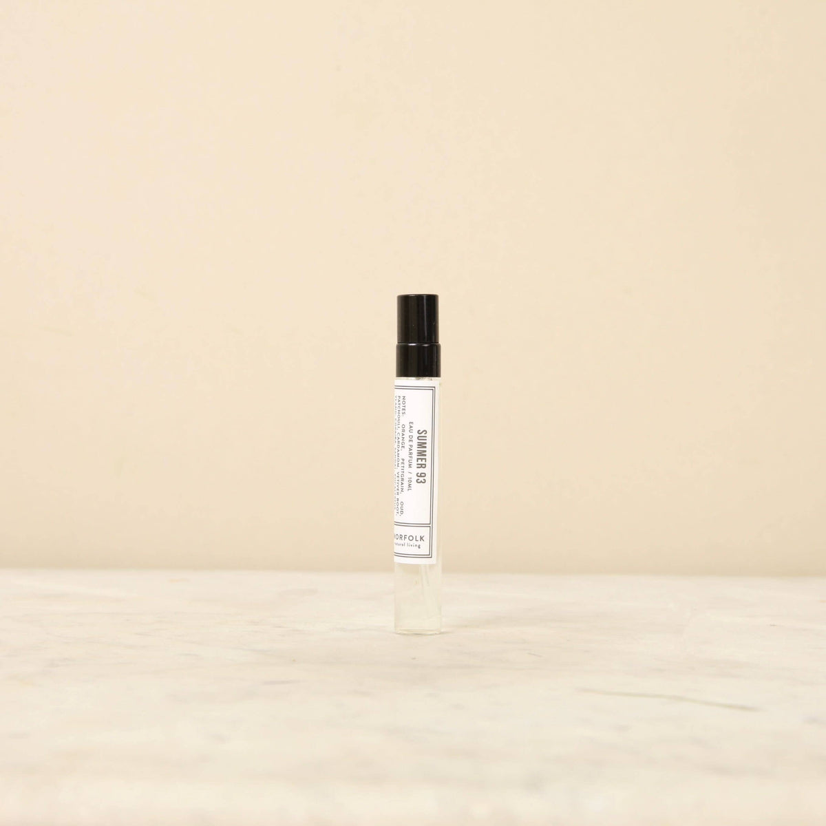 A transparent roll-on Norfolk Natural Living Days of Summer 93 10ml parfum bottle with a black cap, labeled clearly in a simple font, stands upright on a light marble surface against a pale beige background.
