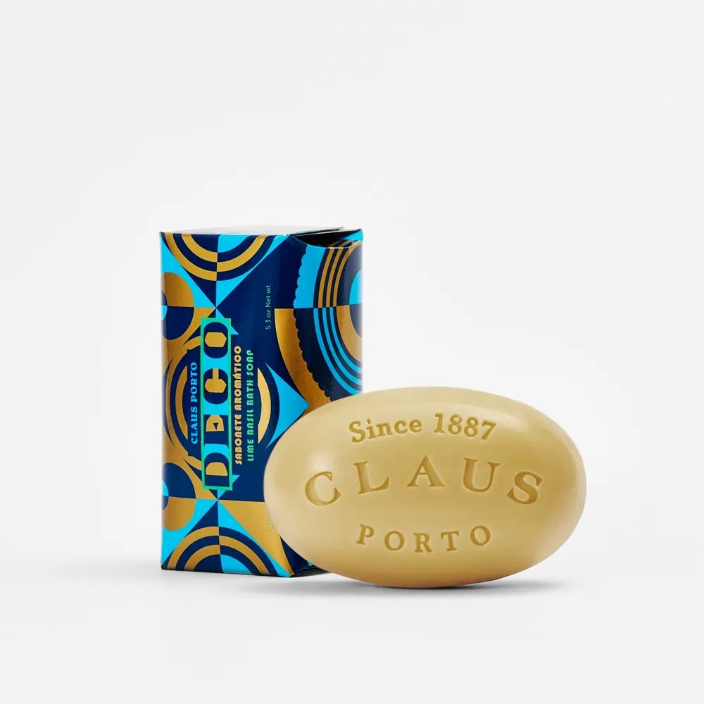 A Claus Porto Deco Lime Basil soap bar in gold beside its colorful Art Deco packaging, marked "since 1887" on the soap.