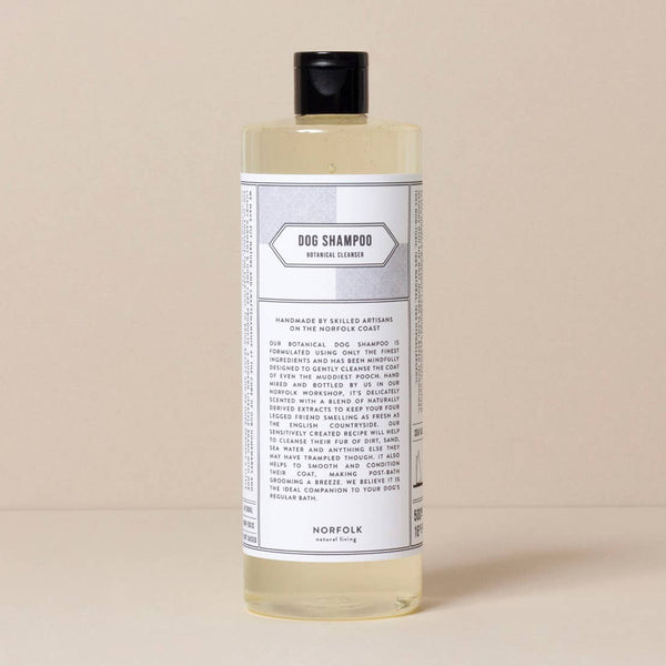 A bottle of Norfolk Natural Living Coastal Dog Shampoo, labeled "dog shampoo, extra cleansing" by Norfolk Natural Living, standing against a light beige background. The label includes detailed text and product information.