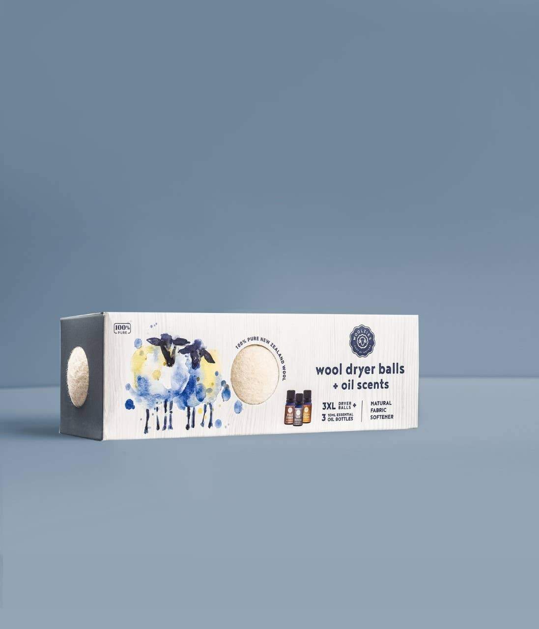 A package of Woolzies Wool Dryer Balls Set of 3 + 3 Laundry Essential oils displayed against a plain blue background, featuring artistic watercolor illustrations of sheep and essential oil bottles.