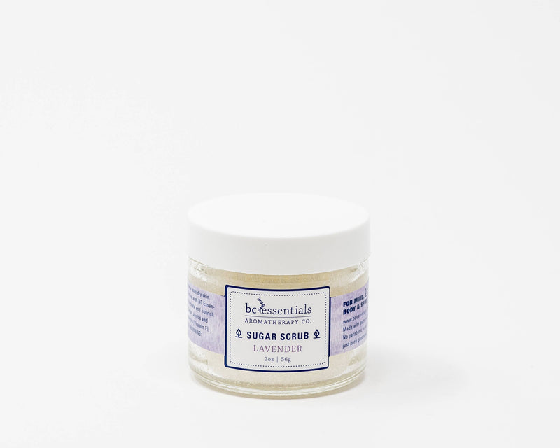 A small, white jar labeled "BC Essentials-Lavender Sugar Scrub - 2oz" by BC Essentials against a plain white background. The jar's label is blue and purple with text detailing the product.