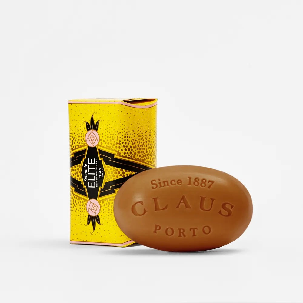 A Claus Porto Elite Tonka Imperial soap bar next to its vibrant yellow and black packaging, featuring intricate designs and the text "since 1887" on both the soap and the box.