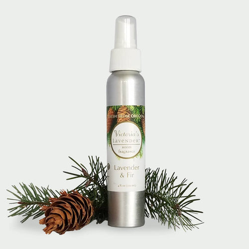 A silver spray bottle labeled "Victoria's Lavender - Lavender & Fir Home Spray" flanked by a pine cone and fir branches against a plain white background.