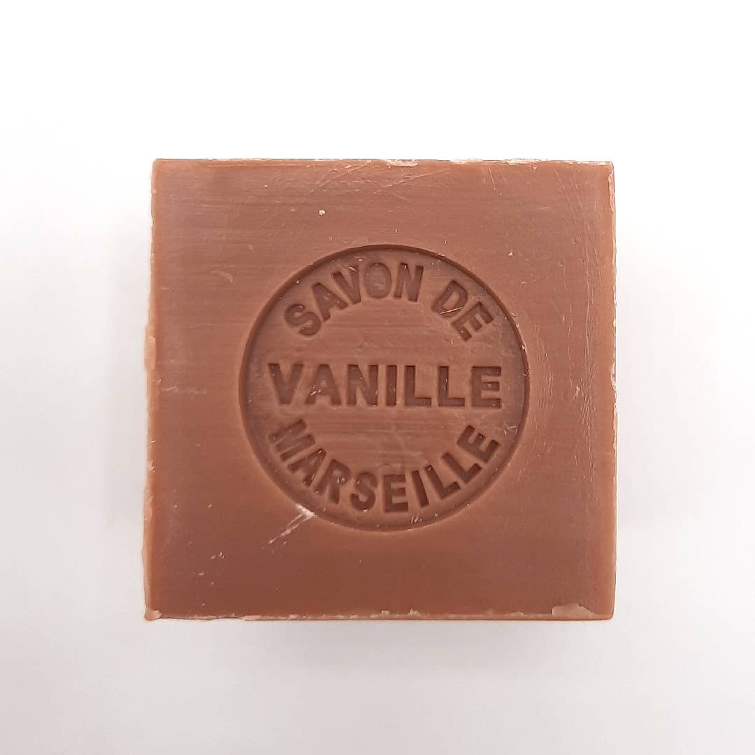 A bar of vanilla-scented Senteurs De France Marseille Vanilla Cube Soap enriched with shea butter, in a light brown color, with embossed text on its surface reading "savon de vanille Marseille." The background is