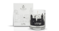 A decorative scented Carthusia Capri Forget Me Not Candle with fig tree essence in a clear glass with black designs, next to its Carthusia I Profumi de Capri white packaging box featuring elegant illustrations and text.
