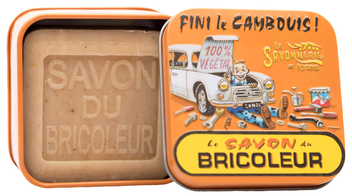 A rectangular La Savonnerie de Nyons Handyman Soap bar labeled "savon du bricoleur" in a tin with a colorful, vintage-style illustration featuring a blue car, bicycle, and the text "100% v.