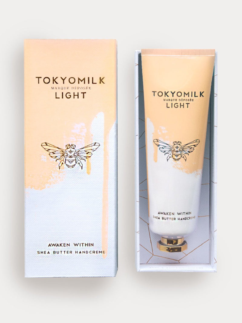 Two Margot Elena TokyoMilk Light Awaken Within No. 02 Shea Butter Handcreme boxes, one in beige with an orange blossom graphic, displayed against a white background.