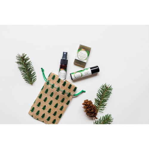 Flat lay of Victoria's Lavender - Lavender & Fir Holiday travel set arranged with pine branches, a pine cone, and a decorated burlap bag on a white background, perfect for a holiday stocking stuffer.