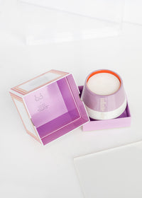 A Infinite She Find Your Fire Ceramic Candle by Margot Elena, in a glass container with a metal lid, placed inside an open purple and white box on a white surface. The box features elegant branding and minimalist design, infused with the aroma of.