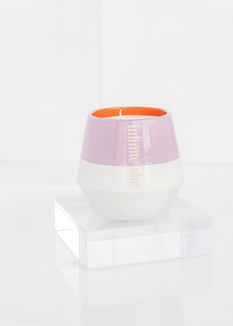 A Margot Elena Find Your Fire Ceramic Candle in an elegant two-tone holder, featuring lilac on the top and white on the bottom, infused with ginger flower aroma, placed on a clear acrylic stand against a white backdrop.