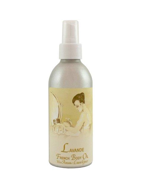 A silver spray bottle of La Bouquetiere Lavender French Argan Body Oil with a vintage-style label depicting a woman sitting at a vanity, applying the oil. The bottle is set against a plain, light