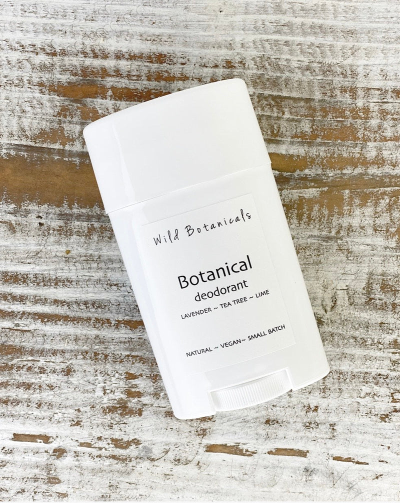 A white stick of Wild Botanicals Lavender Tea Tree Lime aluminum-free deodorant, lying on a weathered wooden surface. The label also indicates the product is natural.