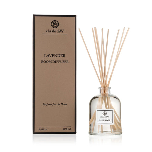 An environmentally friendly Elizabeth W Purely Essential Lavender Diffuser with a clear glass bottle filled with liquid and several reed sticks inserted. Next to it stands its brown packaging box labeled with product details.
