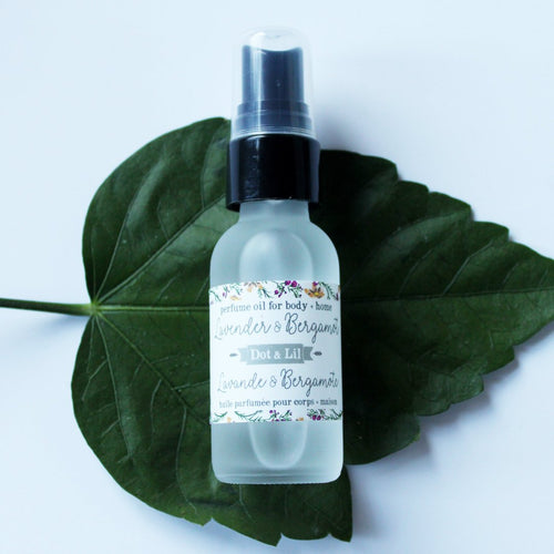 A clear spray bottle of Dot & Lil Lavender + Bergamot Perfume Oil placed on a large green leaf against a white background.