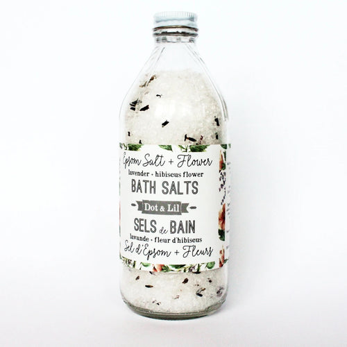 A clear glass bottle filled with Dot & Lil Lavender & Hibiscus Bath Salt, labeled with “epsom salt + flowers” and additional descriptions in both English and French.