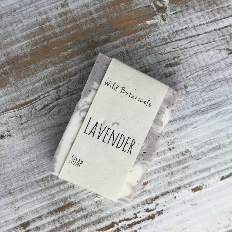 A bar of lavender vegan handmade soap labeled "Wild Botanicals Lavender Soap" by Wild Botanicals on a rustic wooden surface.