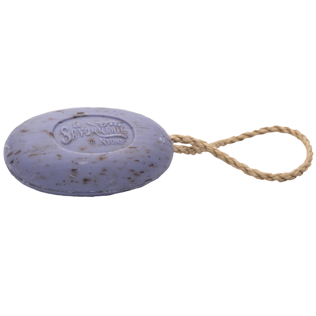 An elliptical, Lavandula angustifolia-colored soap with flecks that exfoliate, featuring embossed lettering "La Savonnerie de Nyons Provence Exfoliating Lavender Soap" on its surface, attached to a braided twine loop, isolated