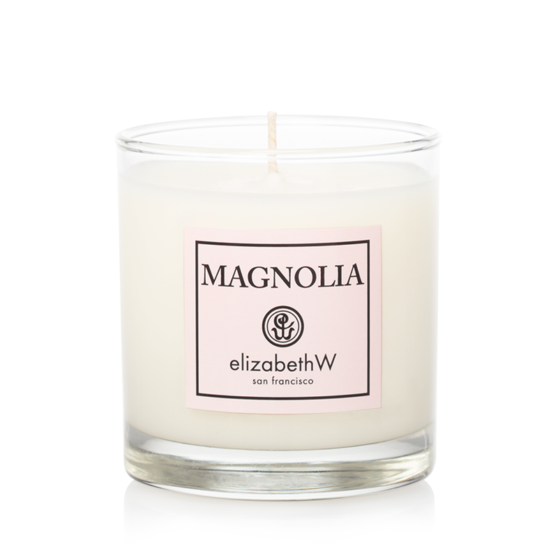 A single elizabeth W Signature Magnolia Candle in a clear glass container with a label that reads "magnolia elizabethw san francisco" featuring a stylized flower logo.
