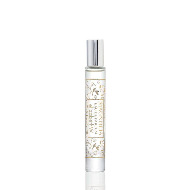 A vertical image displaying a sleek, travel-sized perfume spray bottle with a metallic cap on a white background. The bottle showcases elegant gold floral designs and script text. It is Elizabeth W's elizabeth W Signature Magnolia Rollerball.
