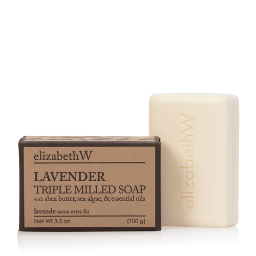 A bar of elizabeth W Purely Essential Lavender Triple-Milled Soap next to its packaging box. The box lists key ingredients like shea butter, sea algae, and essential oils.