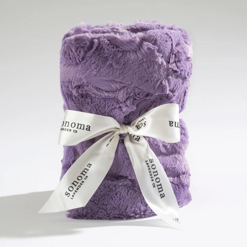 A plush Sonoma Lavender Dusty Plum Heat Wrap with a soft, textured surface, neatly folded and tied with a white ribbon printed with the words "sonoma lavender co." against a light gray background, subtly infused with flax