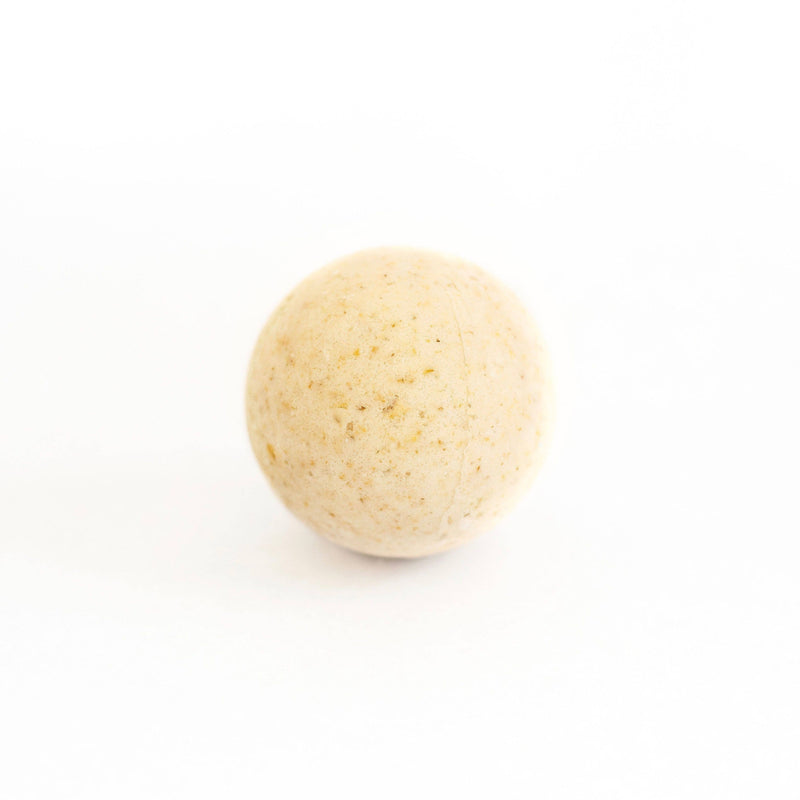 A single beige speckled sphere, resembling a SOAK Bath Co. - Oatmeal Milk and Honey Bath Bomb, is centered on a plain white background, evoking simplicity and minimalism.