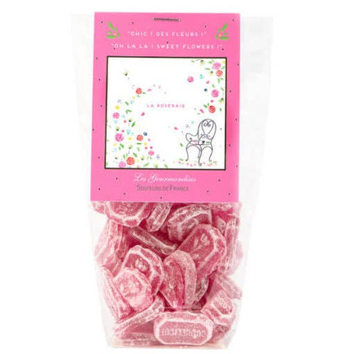 A package of Senteurs De France Versailles Poppies candies in rose garden theme gummy candies with a pink label featuring whimsical text and a simple dog illustration, set against a transparent section showing the pink, poppy-shaped candies
