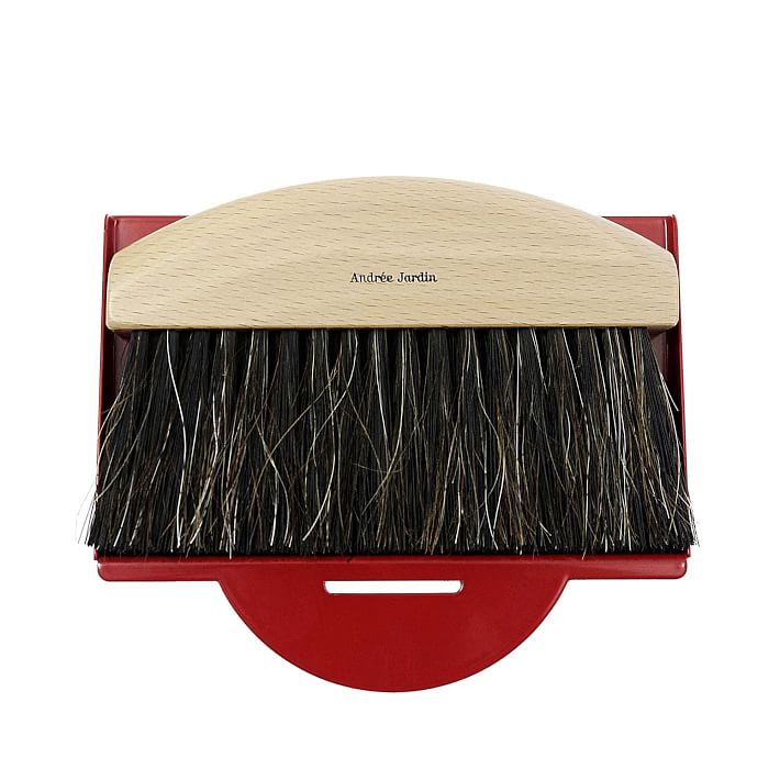 A stylish table crumb collector with a natural wood curved handle labeled "Andrée Jardin" above dense black bristles, set on a vibrant red dustpan.