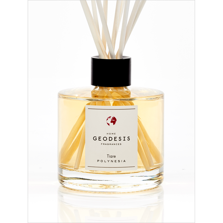 A clear, square glass diffuser bottle labeled "Geodesis Tiare Reed Diffuser" with light yellow liquid and several reed sticks inserted, exuding a Polynesian tiare flower scent, set against a white