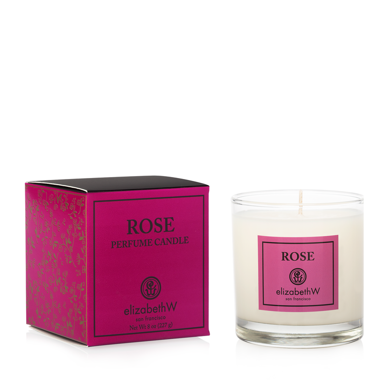A elizabeth W Signature Rose Candle soy wax candle in a clear glass holder, next to its vibrant pink packaging box labeled 'rose'. Both displayed against a white background.