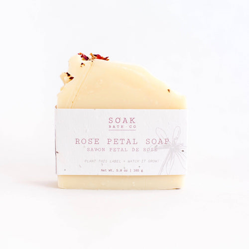 A bar of SOAK Bath Co. - Rose Petal Soap wrapped in biodegradable seed paper from SOAK Bath Co., with the label stating “plant this label. watch it grow!” against a white background.
