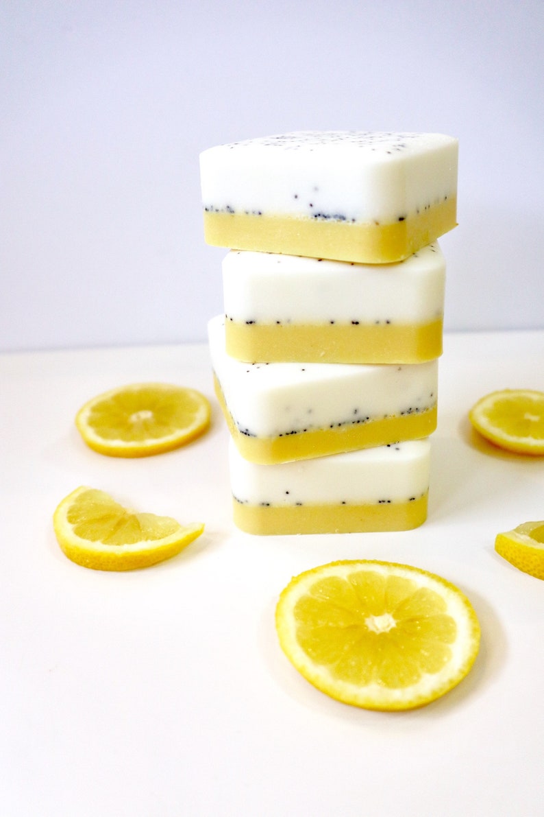 A stack of four Homegrown {77833} Co - My Main Squeeze goat's milk bath bars with vibrant yellow lemon slices arranged on a white surface against a plain background.