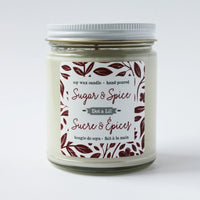 A Dot & Lil Sugar + Spice Soy Candle in a clear glass jar labeled with decorative leaf and hand motifs. The text also mentions it is hand-poured.