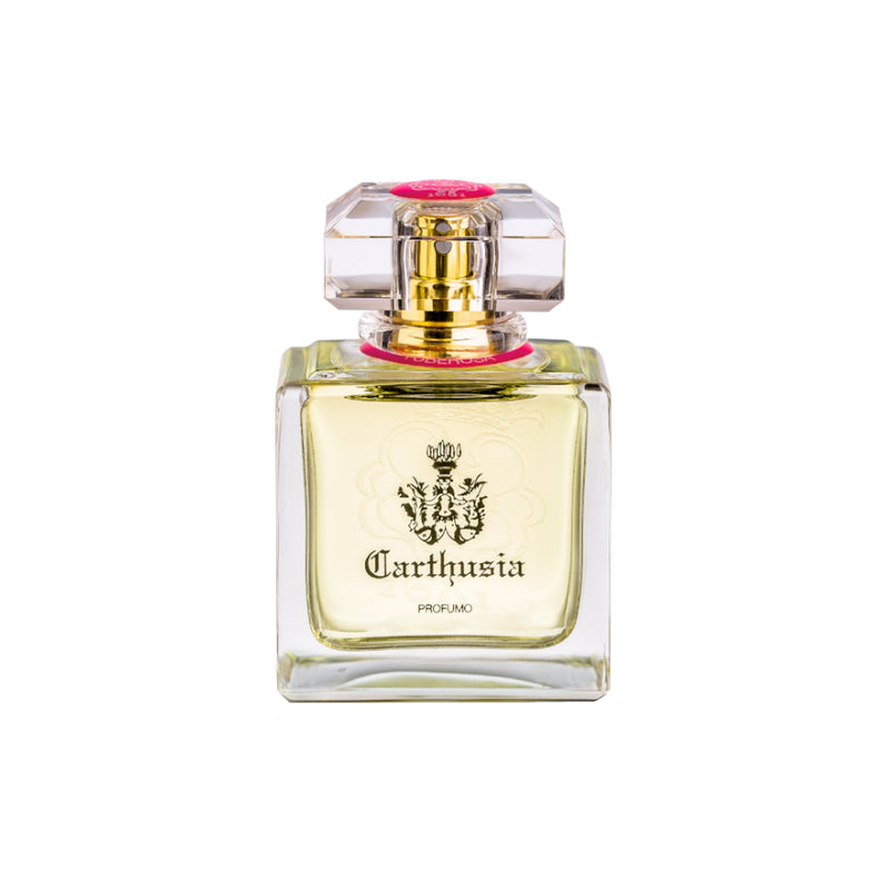 A clear glass perfume bottle with a royal crest labeled "Carthusia I Profumi de Capri." The bottle has a square base, translucent yellow liquid inside, and a pink cap with a faceted top that hints