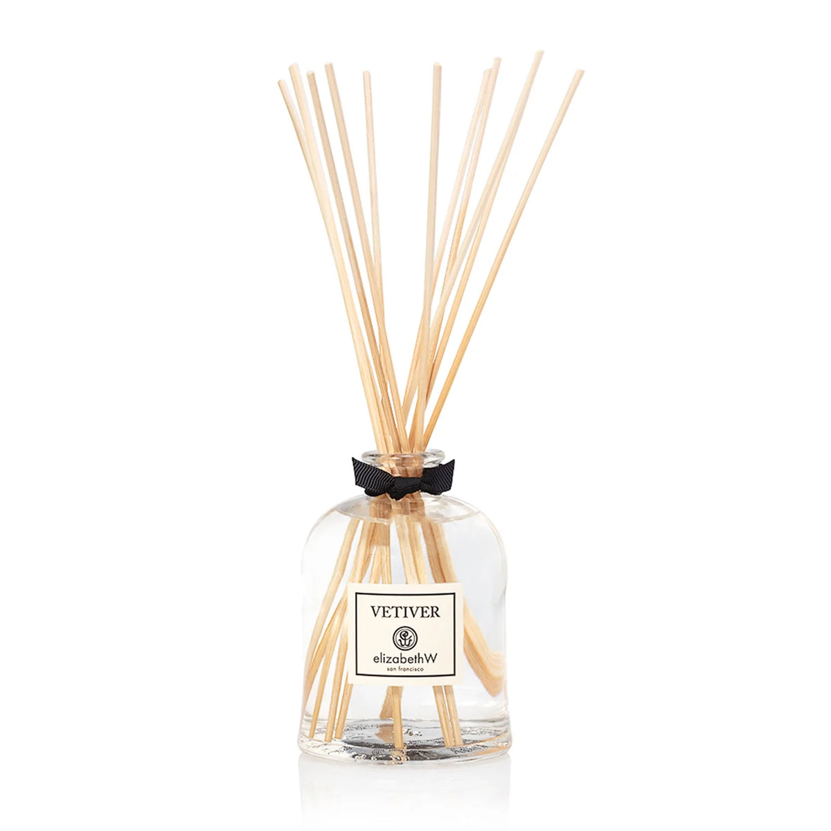 An Italian glass diffuser bottle labeled "elizabeth W Signature Vetiver Diffuser" with several light brown reed sticks inserted, and a decorative black bow tied around the neck, against a white background.