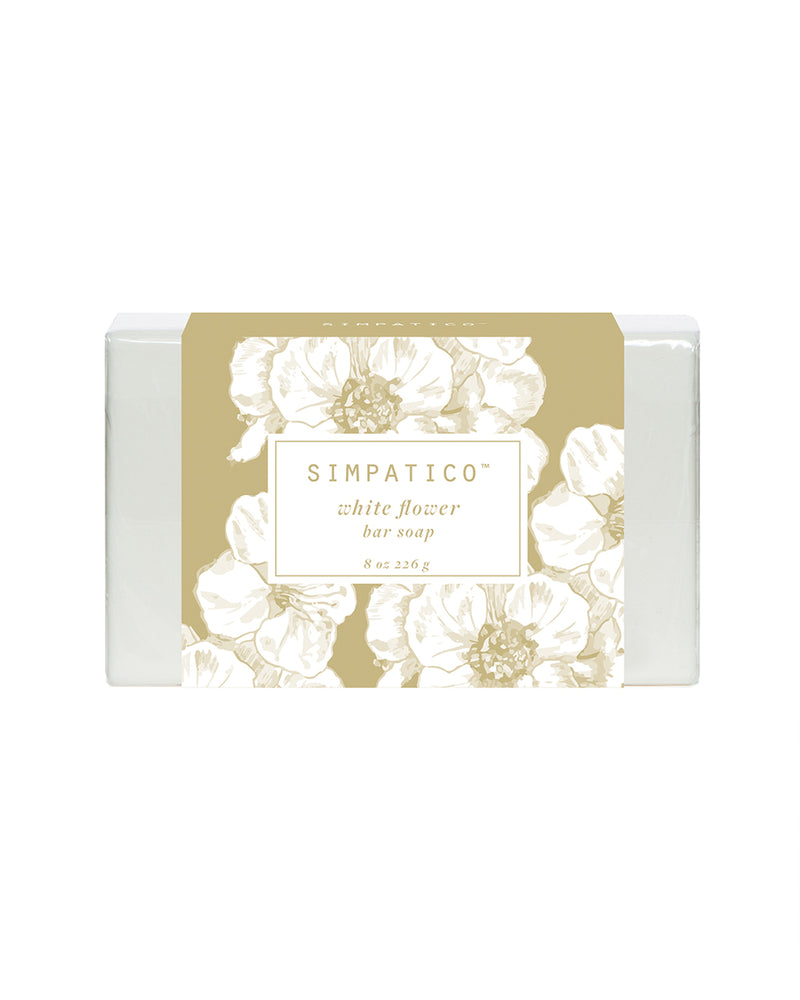 A bar of Simpatico White Flowers Bar Soap, with the scent of simpatico white flowers, in beige packaging adorned with elegant white floral patterns. The label mentions "8 oz 226 g" on a.