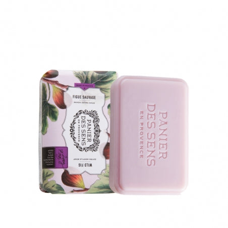 A bar of pink soap labeled "Panier Des Sens Extra-Soft Vegetable Soap - Wild Fig" next to its packaging, which features illustrations of figs and the text "Figue Sauvage." The packaging is purple and white.