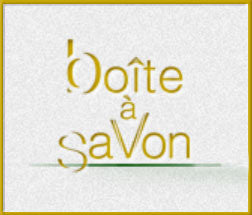 Text logo with stylized writing: "boîte à savon". The letters are creatively arranged with some altered shapes, set against a textured background, enclosed in a thin yellow border.