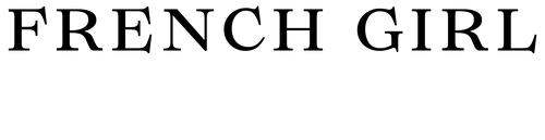 A black cat with wide eyes lies on its side on a wooden floor, looking up curiously. Its tail is stretched out and its white whiskers stand out against its dark fur.