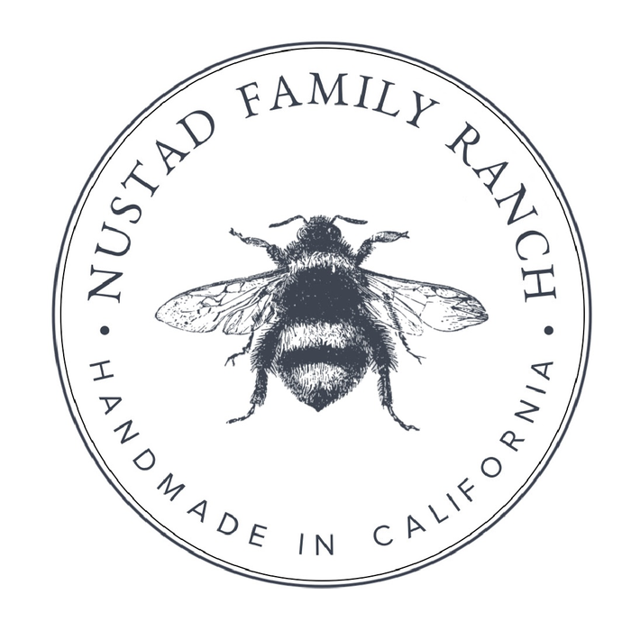 Circular logo of Nustad Family Ranch featuring a detailed illustration of a bee at the center, encircled by text "Nustad Family Ranch" and "Handmade in California.