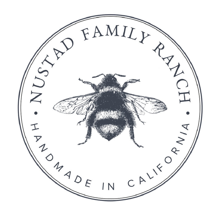 Logo of Nustad Family Ranch featuring a detailed illustration of a bee centered within a circular frame with the text "Nustad Family Ranch" and "Handmade in California.